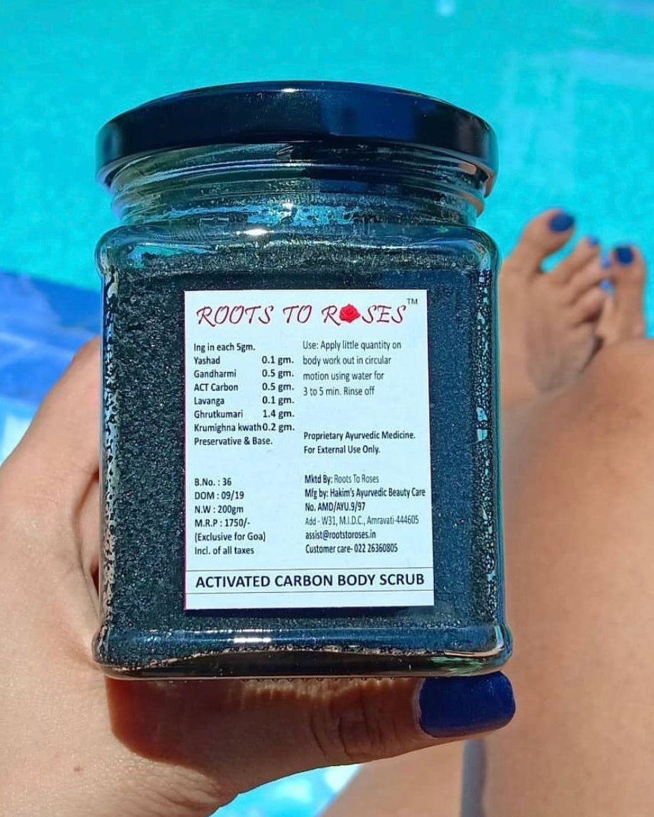 A jar of Activated Carbon Body Scrub is held by a person with a toes tattoo, with a pool and blue sky in the background.