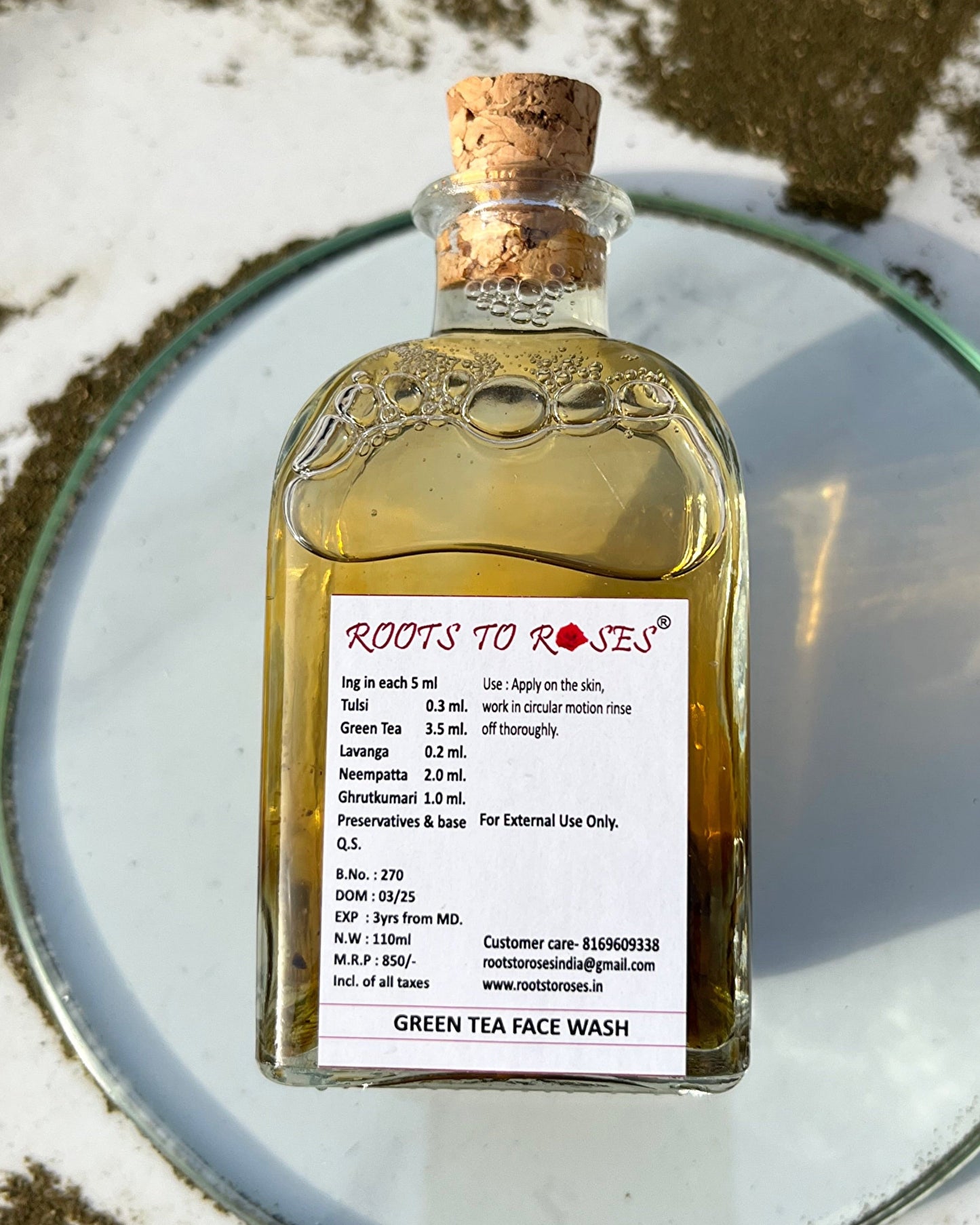 Bottle of 'Roots to Roses' Green Tea Face Wash on a reflective surface with a natural background.