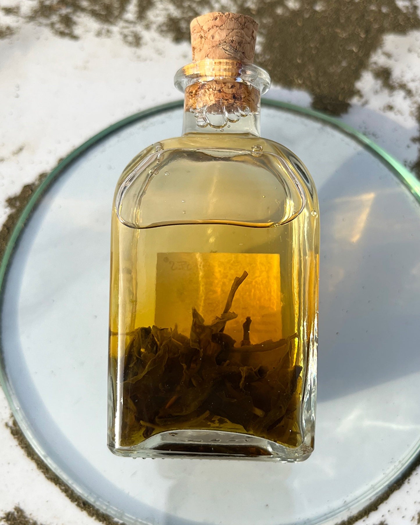 Glass bottle with cork lid containing a yellow liquid on a reflective surface