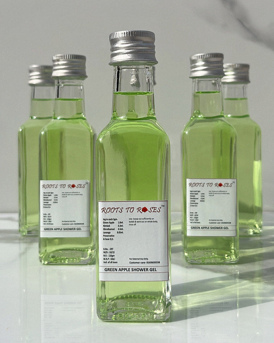 Three transparent glass bottles with green liquid inside, labeled as 'Green Apple Brightening Shower Gel'. They are placed on a surface with a shadow falling over part of the image.