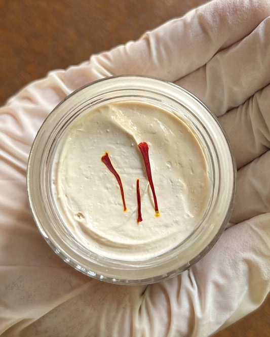 Container of cream with two red sticks on a wooden surface, held by a gloved hand.